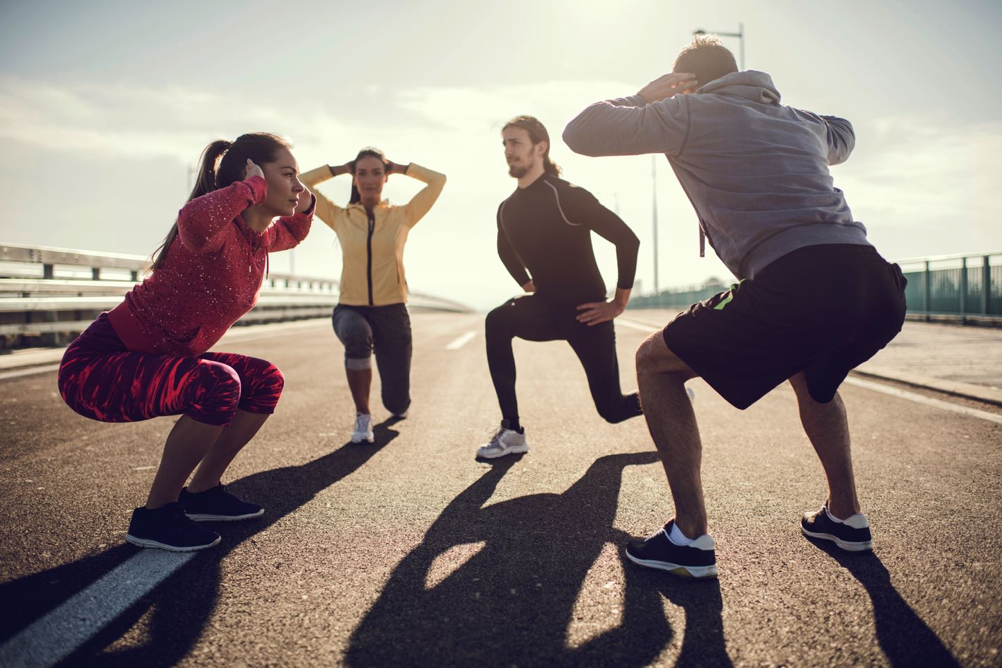 Team of young athletes exercising outdoors while doing squats and stretching exercises.