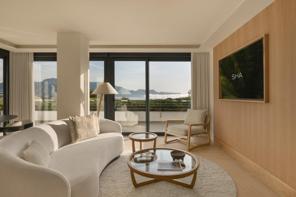 legant living room at SHA Spain wellness hotel, featuring warm wooden walls, white sofas and large windows with views of the sea and mountains.