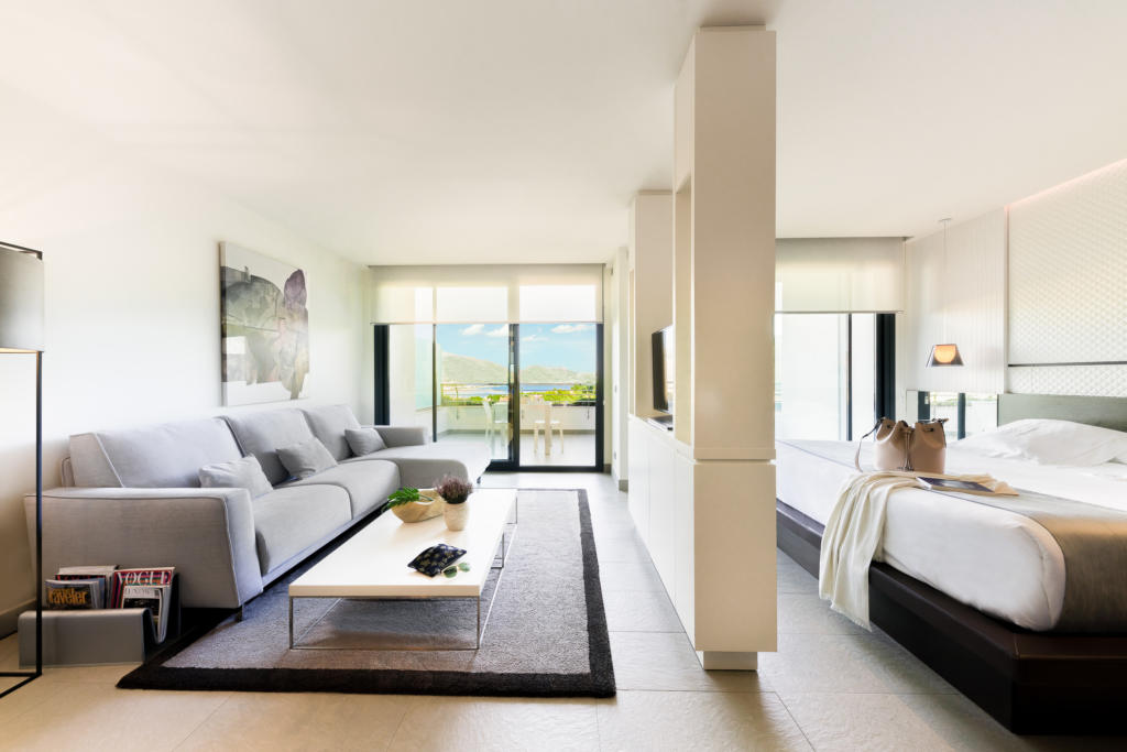 Spacious suite at SHA Spain featuring a living area, luxurious bed and large windows that flood the neutral-toned space with natural light.